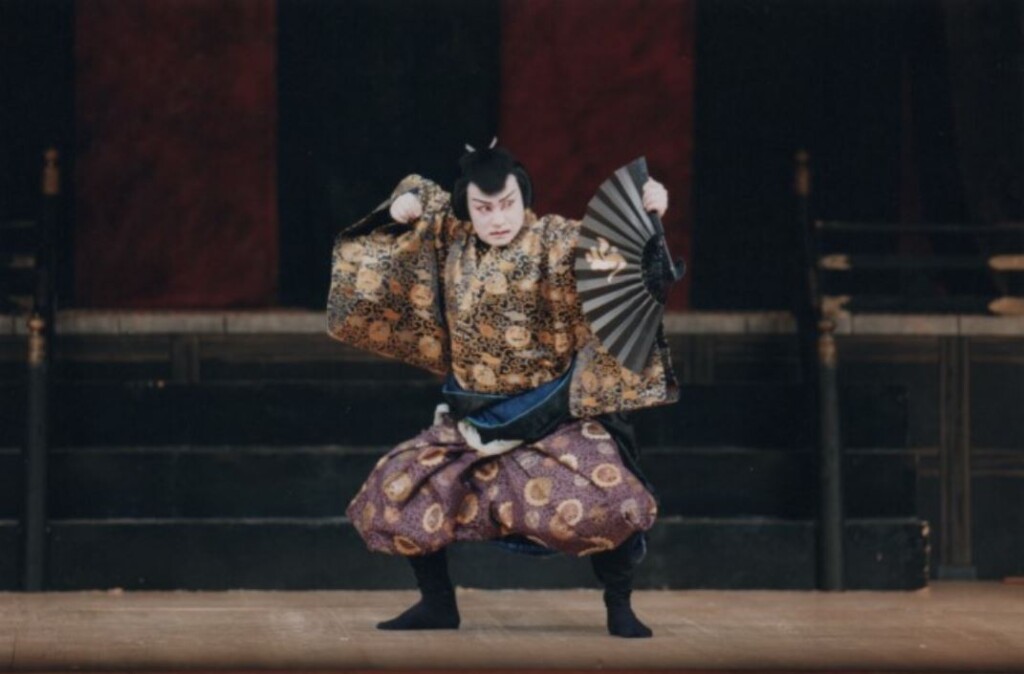扇を手に腰を落として構える男踊りの踊り手